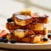 Golden Brown French Toast Stack Dusted With Powdered Sugar, Fresh Berries, And Maple Syrup On A White Plate