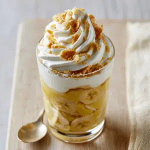Layered Banana Cream Pudding In A Clear Glass With Custard, Banana Slices, Whipped Cream, And Crushed Wafers